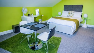 Une chambre à coucher de taille modeste, comprenant un lit, des tables de chevet, un bureau avec des chaises et une moquette verte.