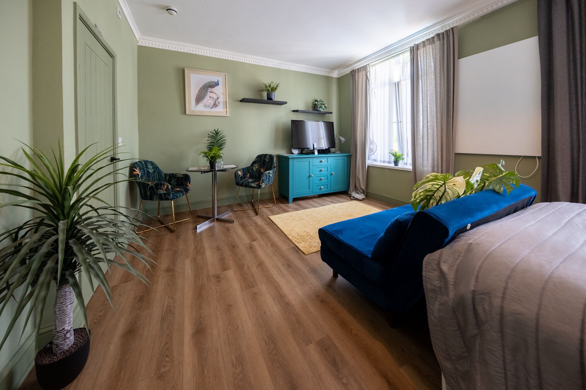 Habitació d'hotel amb llit, escriptori amb cadira, televisió i finestra amb cortines.