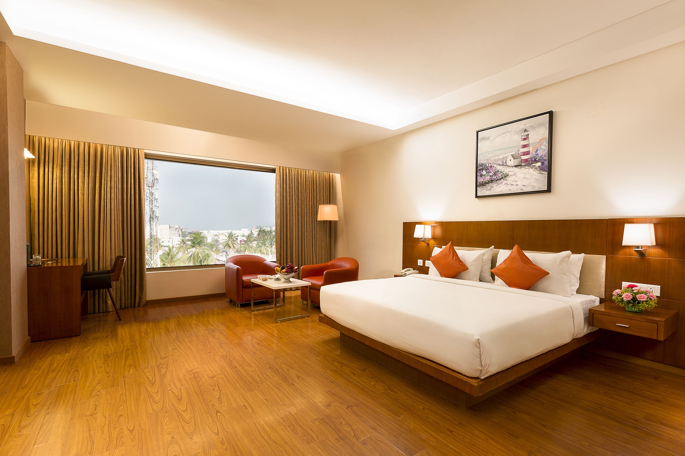 A hotel room with a large bed, two chairs, a small table, a desk, and a nightstand.