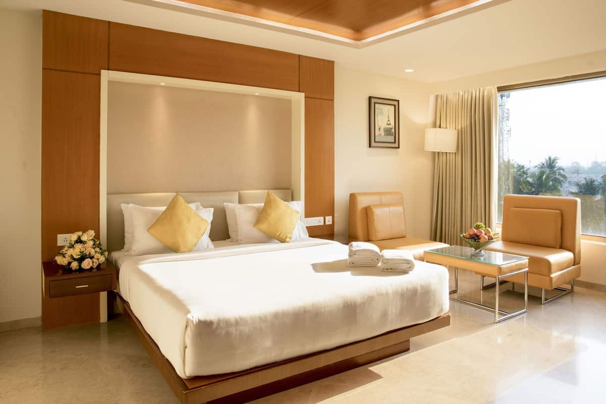 A hotel room with a large bed, a glass coffee table, a sofa, and a view of the outdoors.
