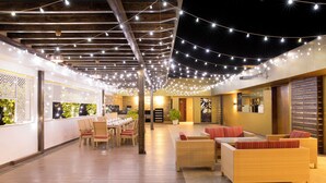 A spacious indoor area with a long dining table, wicker sofas, and string lights. - CJ Pallazzio (Salem)