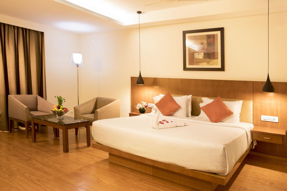 A hotel room with a large bed, two armchairs, a small table with fruit, and a wall-mounted picture.