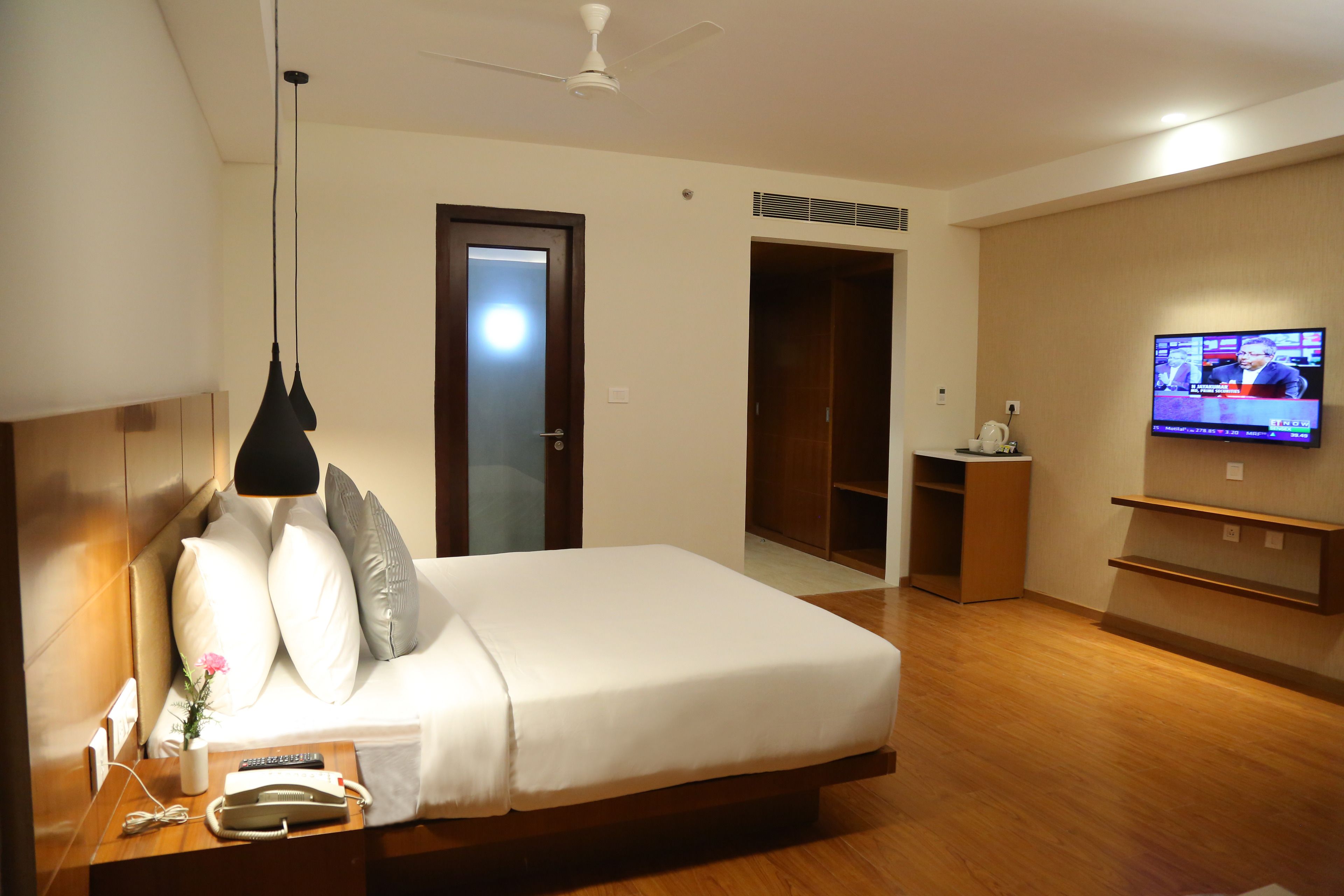 A hotel room with a bed, bedside table, TV, wardrobe, and a ceiling fan.