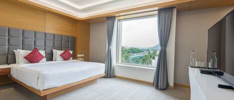 A modern hotel room with a large bed, a desk, and a large window offering a city view.