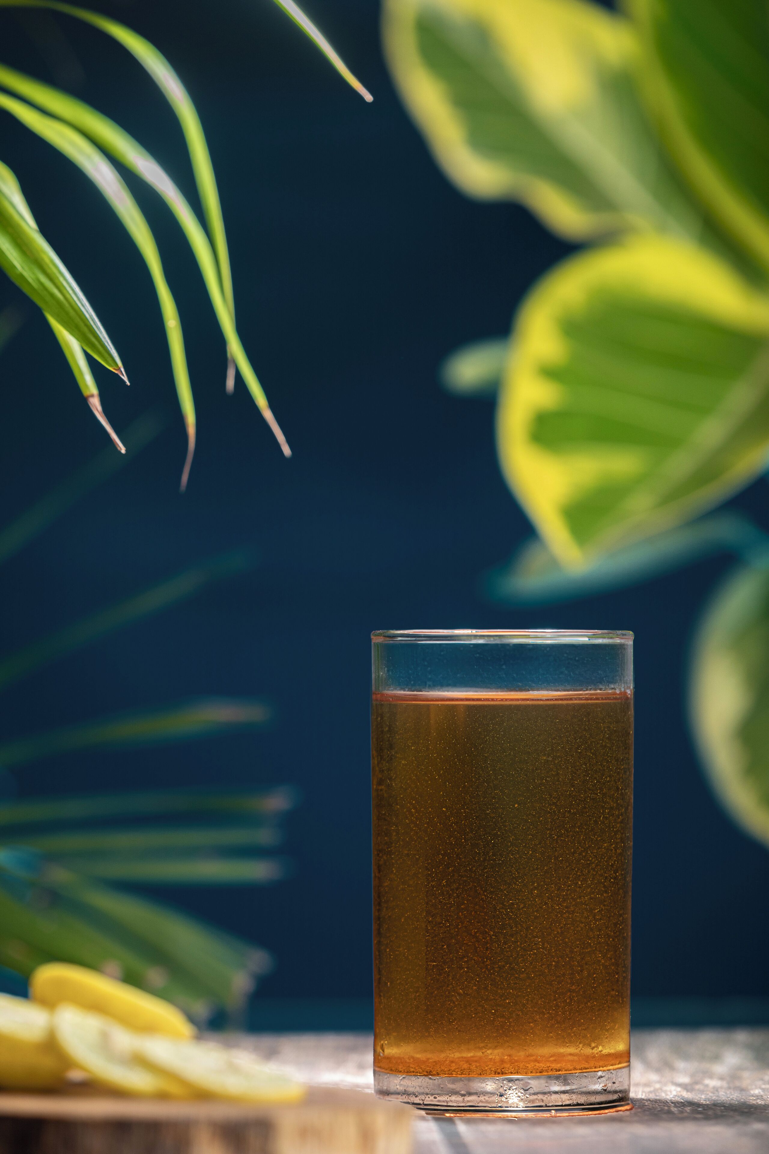 A glass of amber liquid on a wooden surface with green leaves in the background.