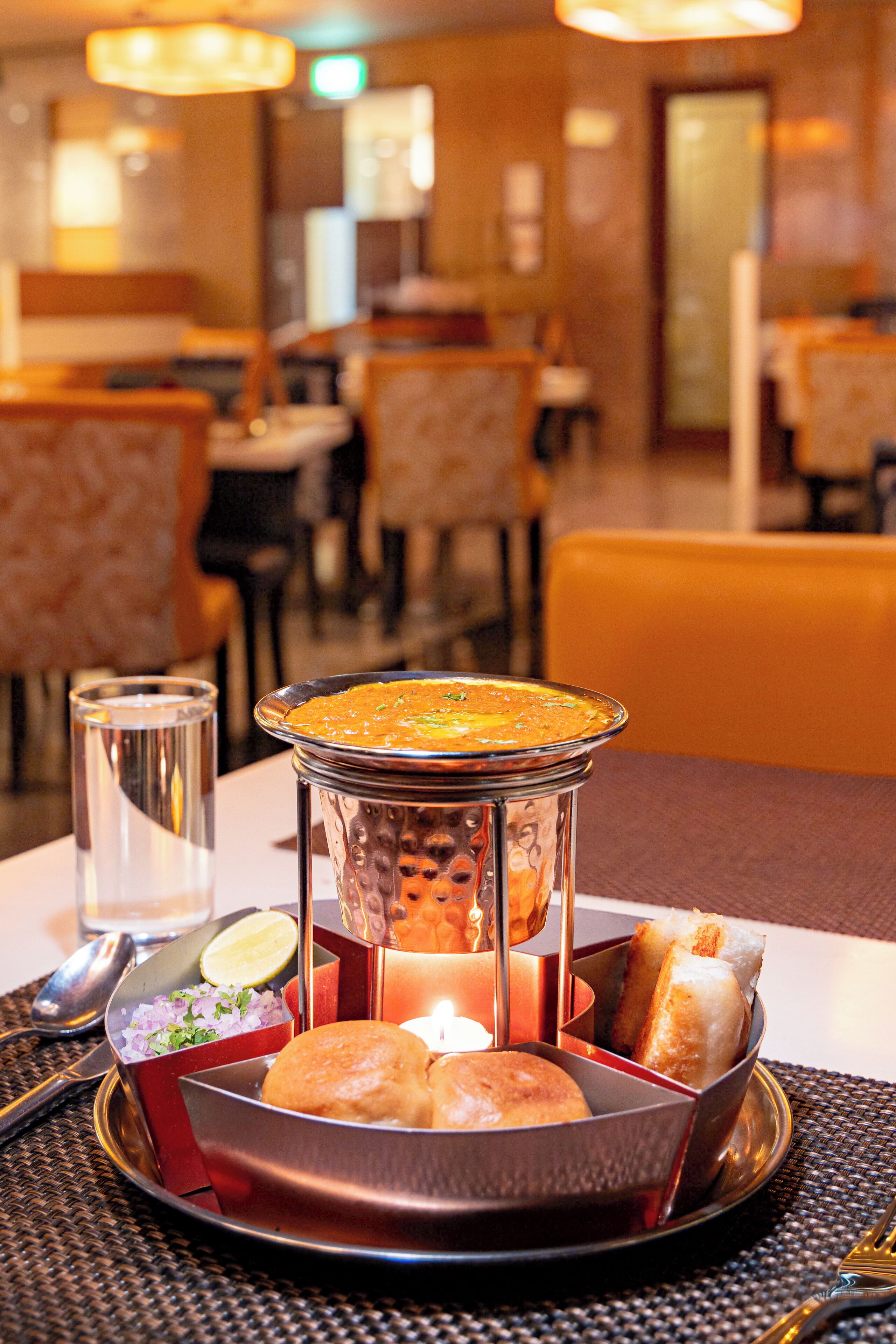 A dining table with a candle, a glass of water, and a plate with bread and a bowl of soup.