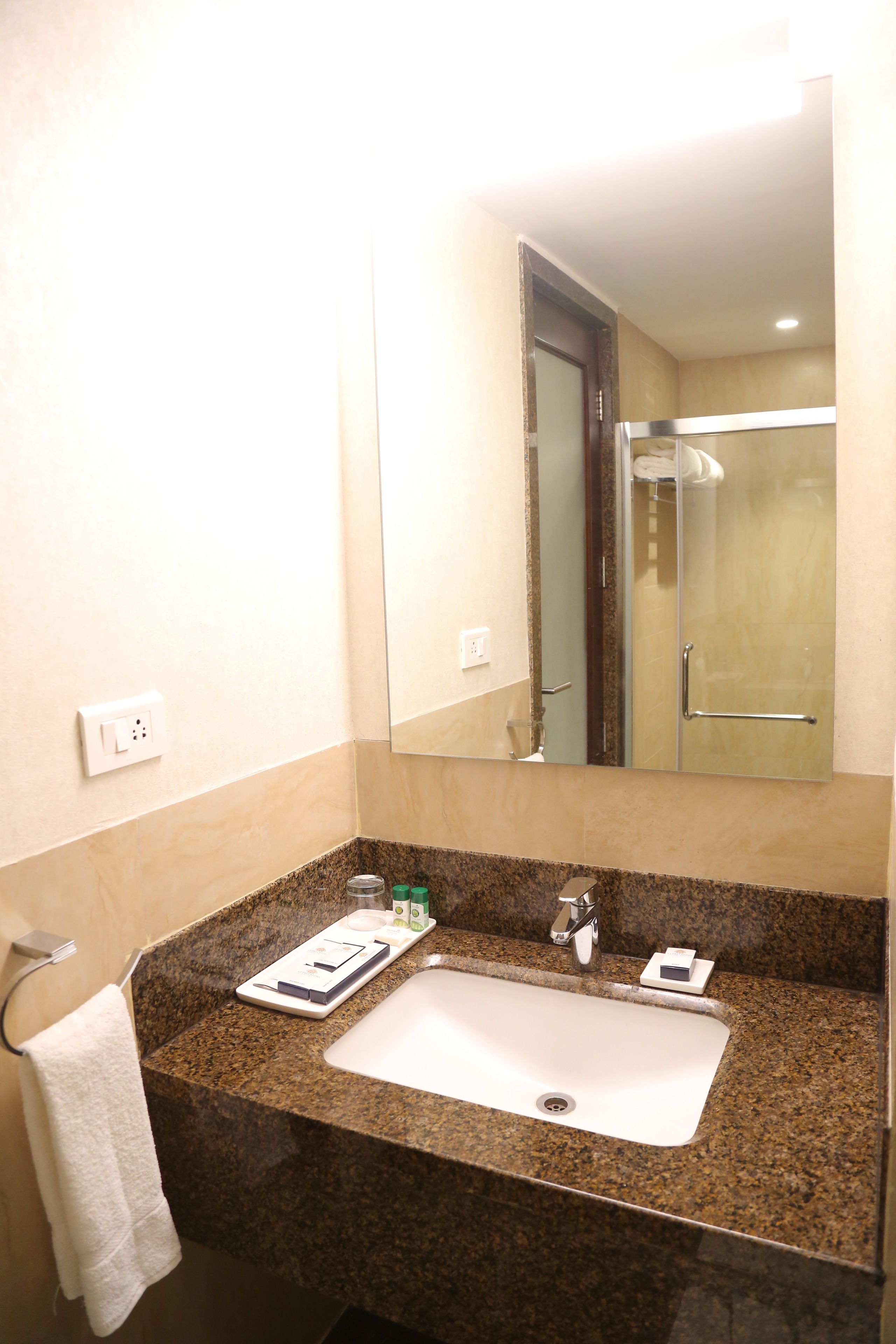Une salle de bain avec un comptoir en granit, un lavabo blanc, un miroir et une serviette suspendue à un porte-serviettes.
