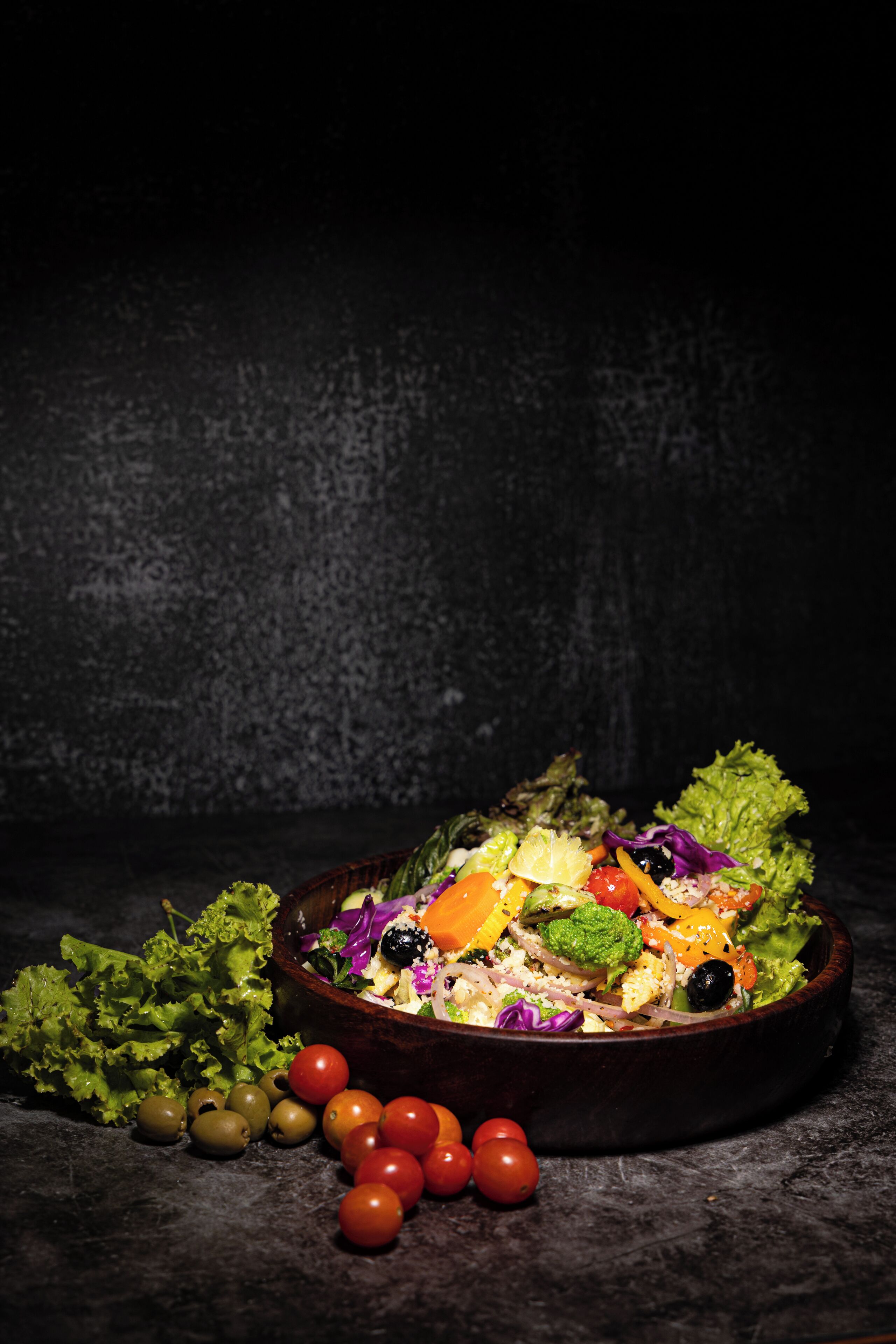 Un tazón de ensalada colorida con diversas verduras y aceitunas, sobre una superficie oscura.