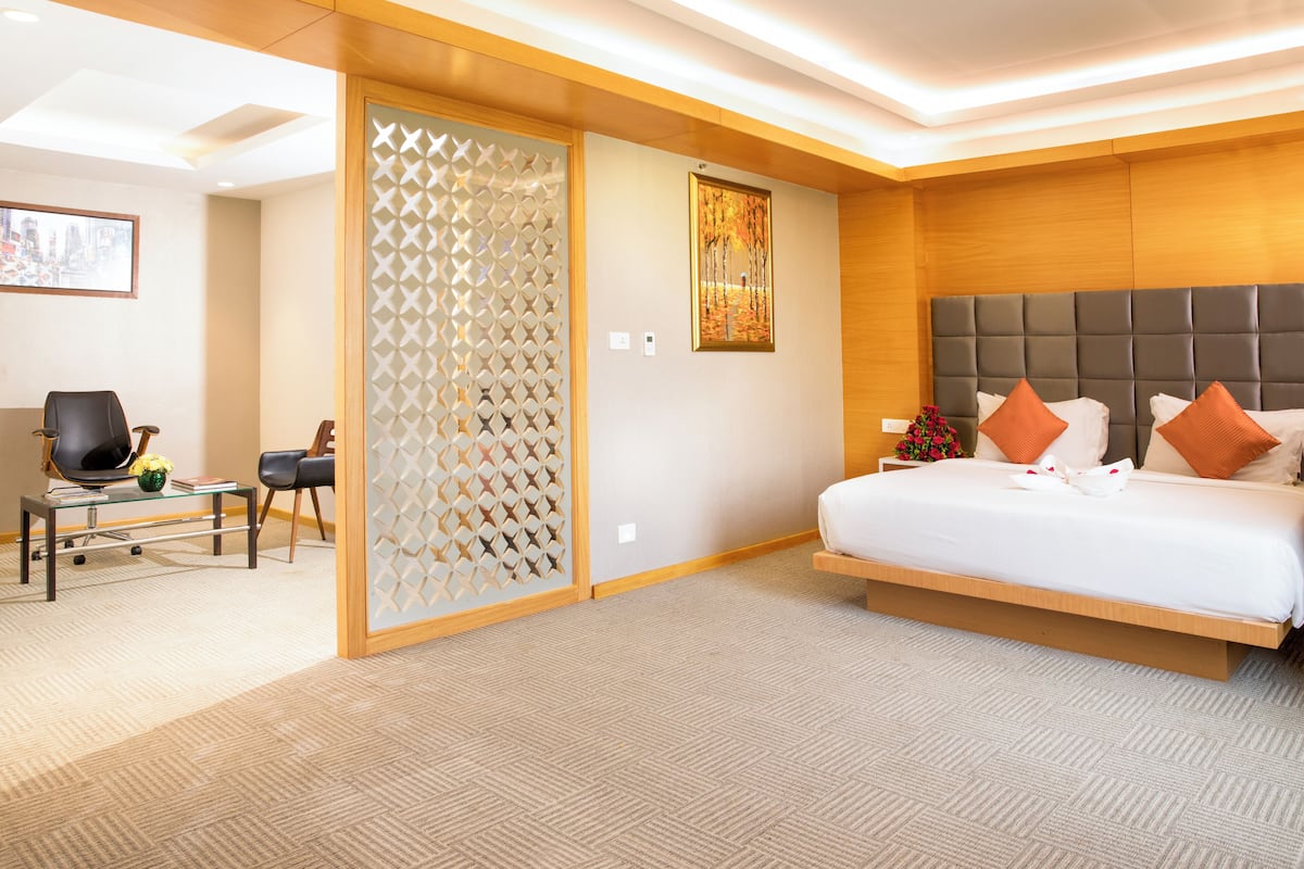 A modern hotel room with a large bed, a desk with a chair, and a decorative partition.