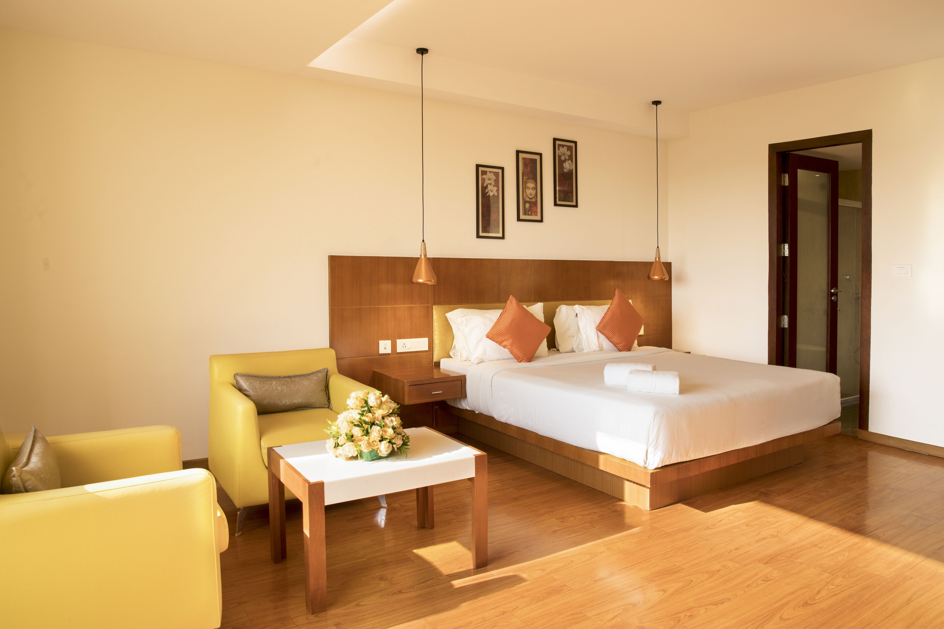 A hotel room with a large bed, a bedside table with a vase of flowers, a yellow armchair, and a wooden floor.