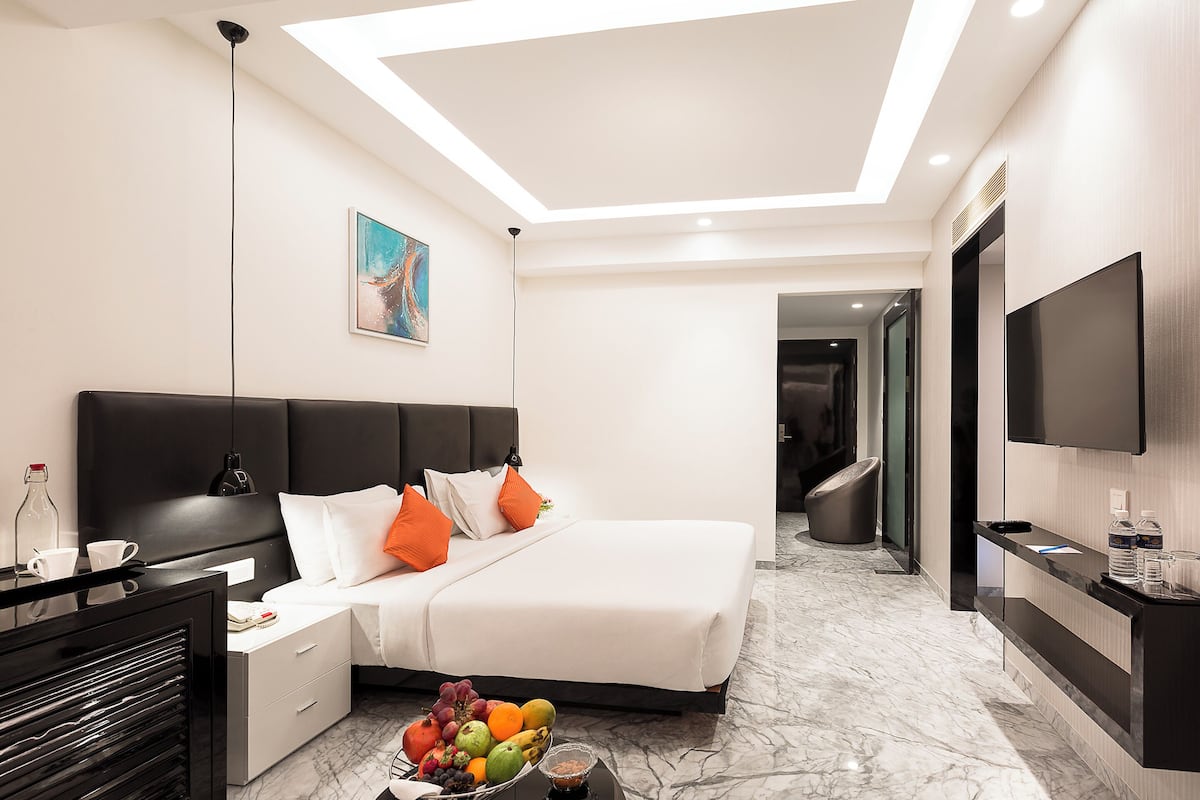 A modern hotel room with a large bed, a desk, a flat-screen TV, and a fruit bowl on the nightstand.