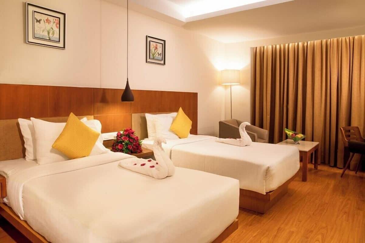 A hotel room with two beds, a wooden headboard, a bedside table with a lamp, a chair, and a curtain.