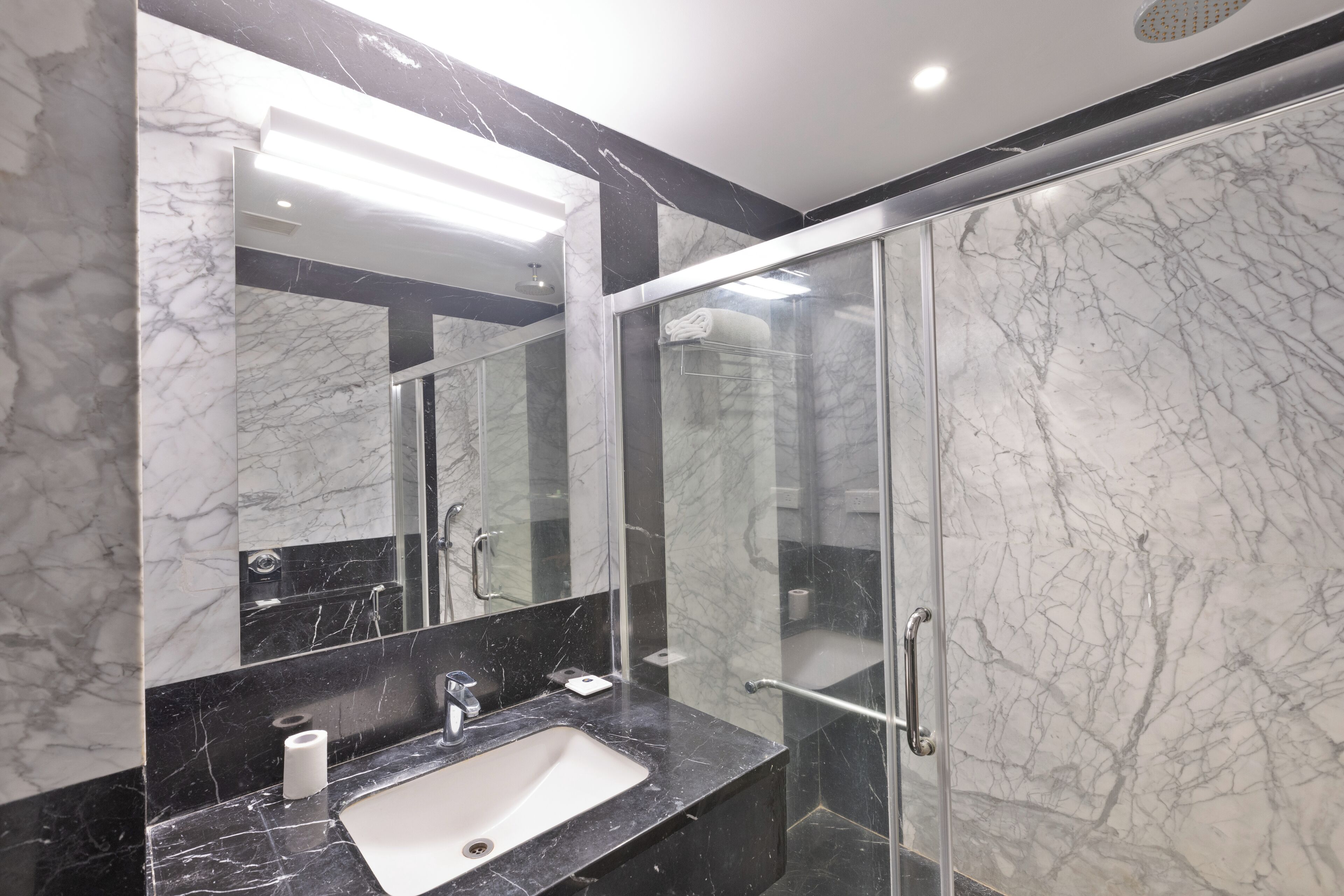 A modern bathroom with a marble sink, a large mirror, and a glass shower enclosure.