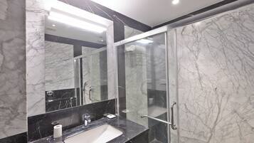 A modern bathroom with a marble sink, a large mirror, and a glass shower enclosure.