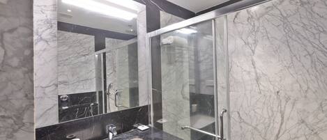 A modern bathroom with a marble sink, a large mirror, and a glass shower enclosure.
