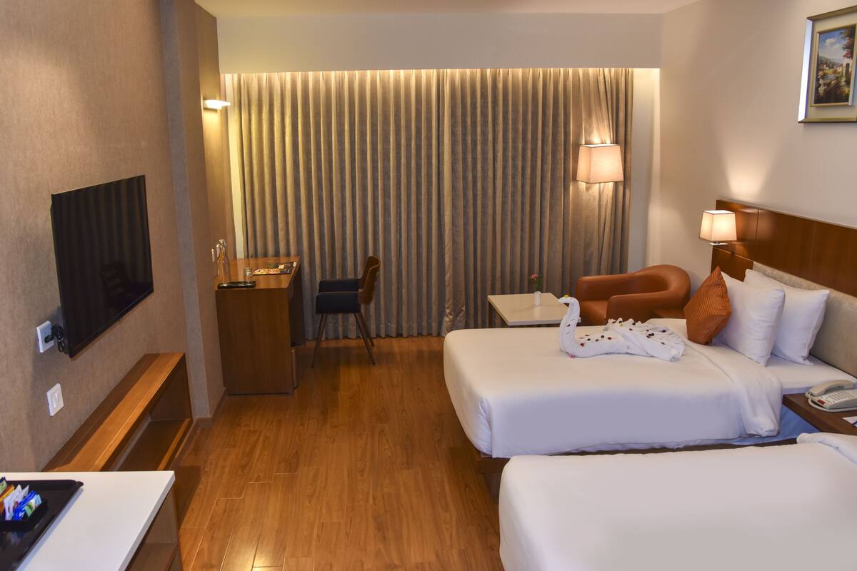 A hotel room with two beds, a desk, a chair, a TV, and a window with curtains.
