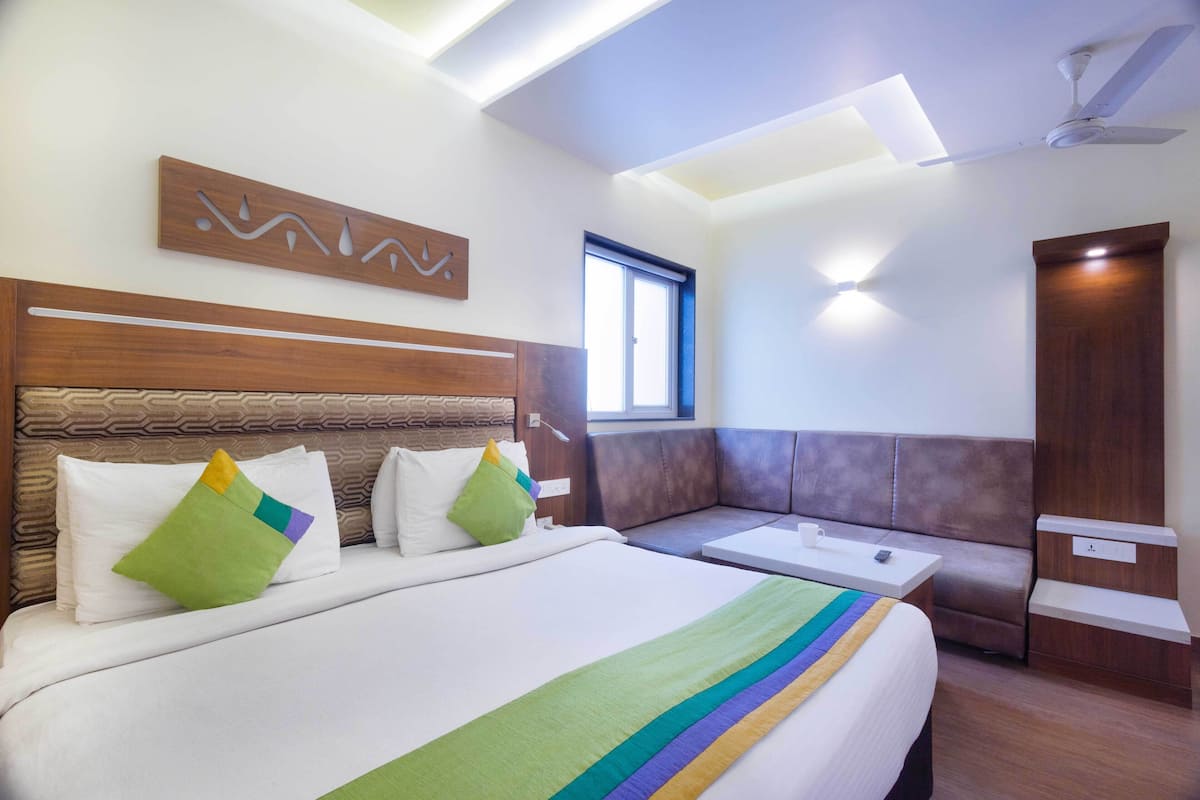 A hotel room with a large bed, a sofa, a small table, and a ceiling fan.
