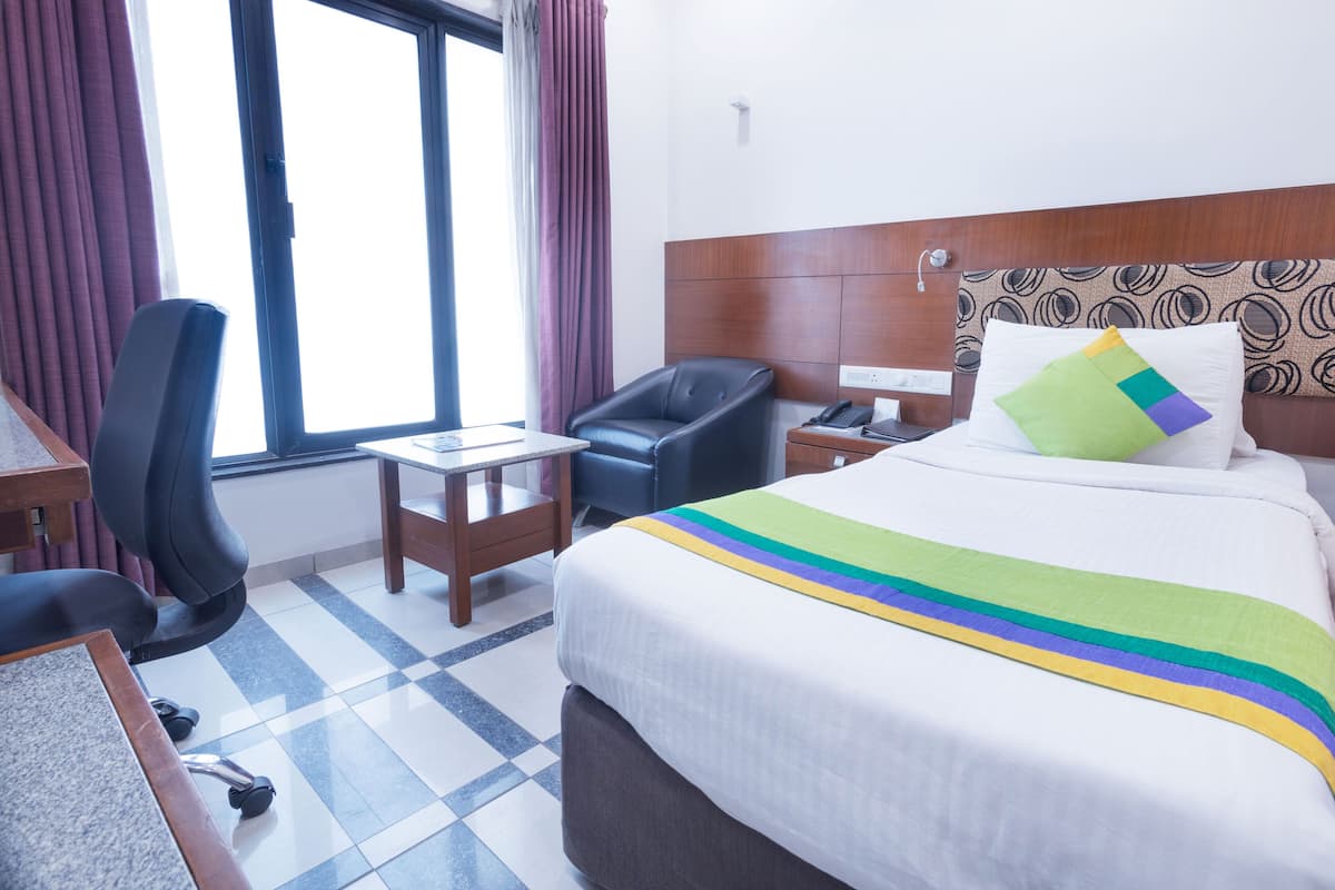 A hotel room with a bed, a desk, a chair, and a window with curtains.