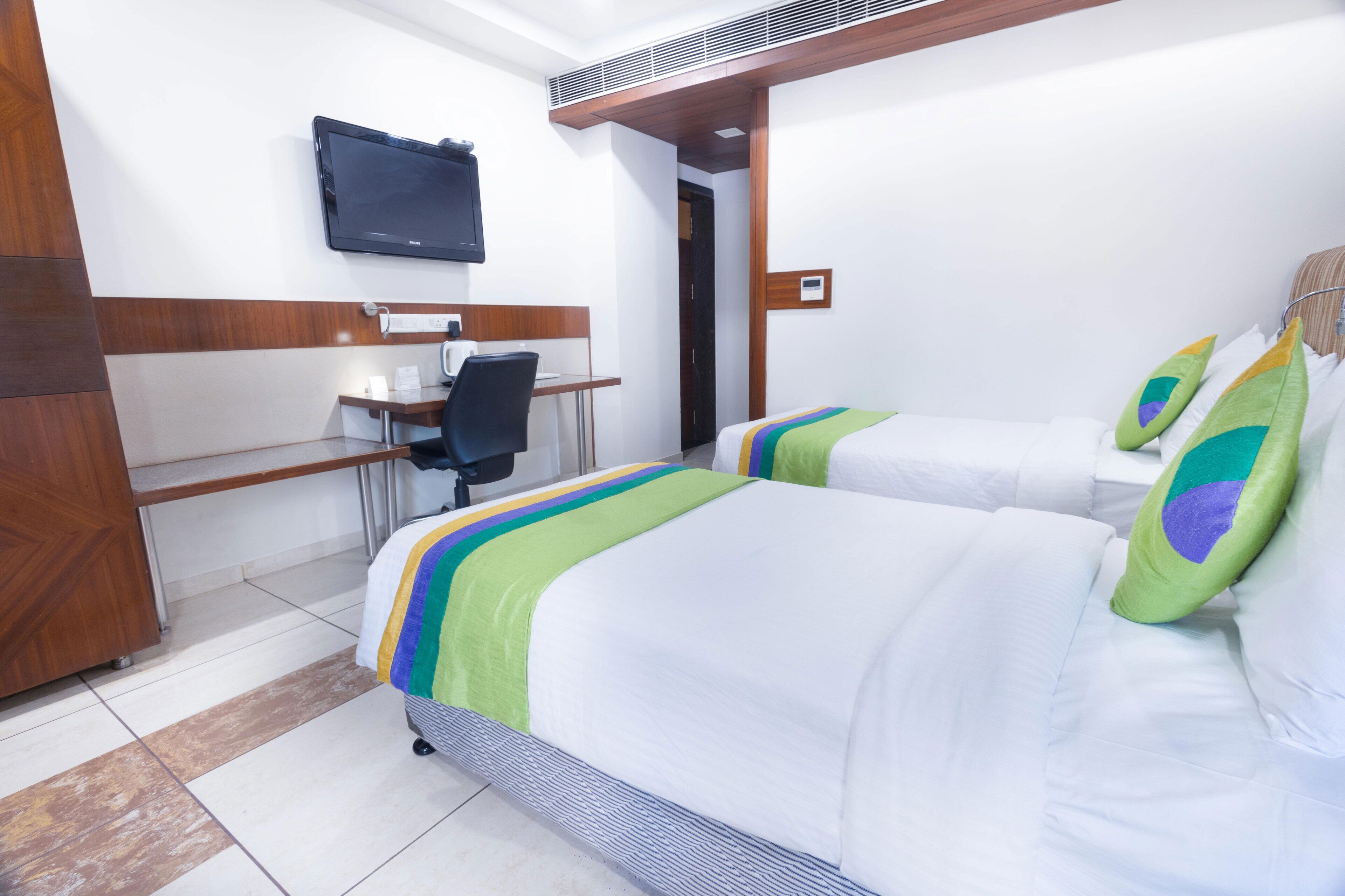 A hotel room with two beds, a desk with a chair, a television, and a wooden wardrobe.