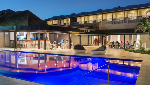 A swimming pool with a blue-lit edge, outdoor seating, and a bar area.