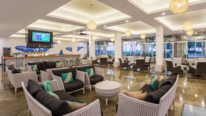 A spacious lobby with modern furnishings, a bar area, and large windows offering a view of the outdoors.
