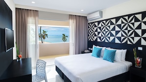 A modern hotel room with a large bed, a TV, a desk, and a view of the ocean.