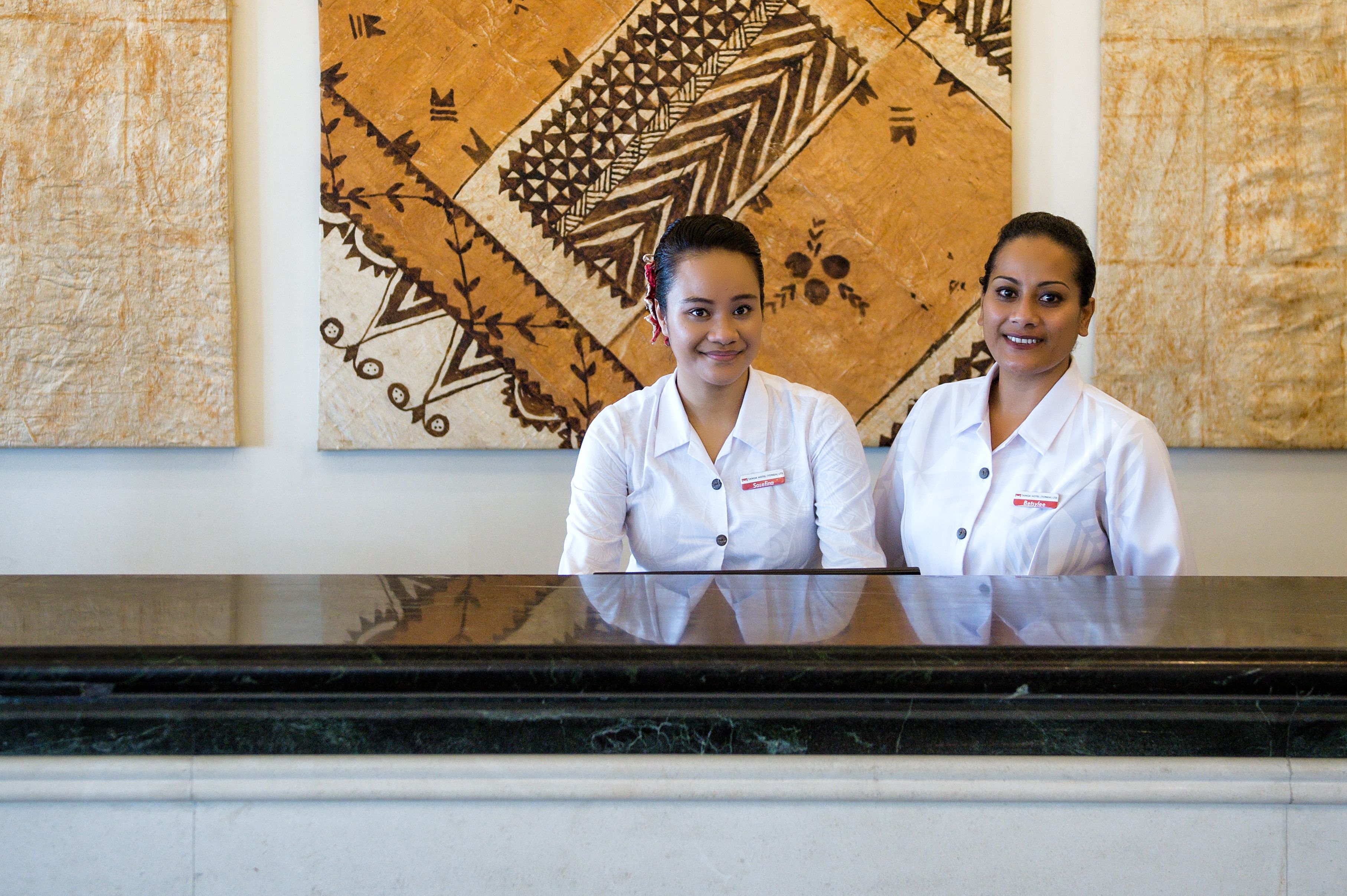 Dos recepcionistas en la recepción de un hotel, con un amplio mural decorativo al fondo.