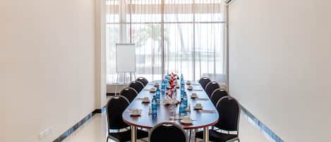 Une salle de conférence avec une longue table, des chaises, un tableau blanc et une grande fenêtre avec des rideaux.