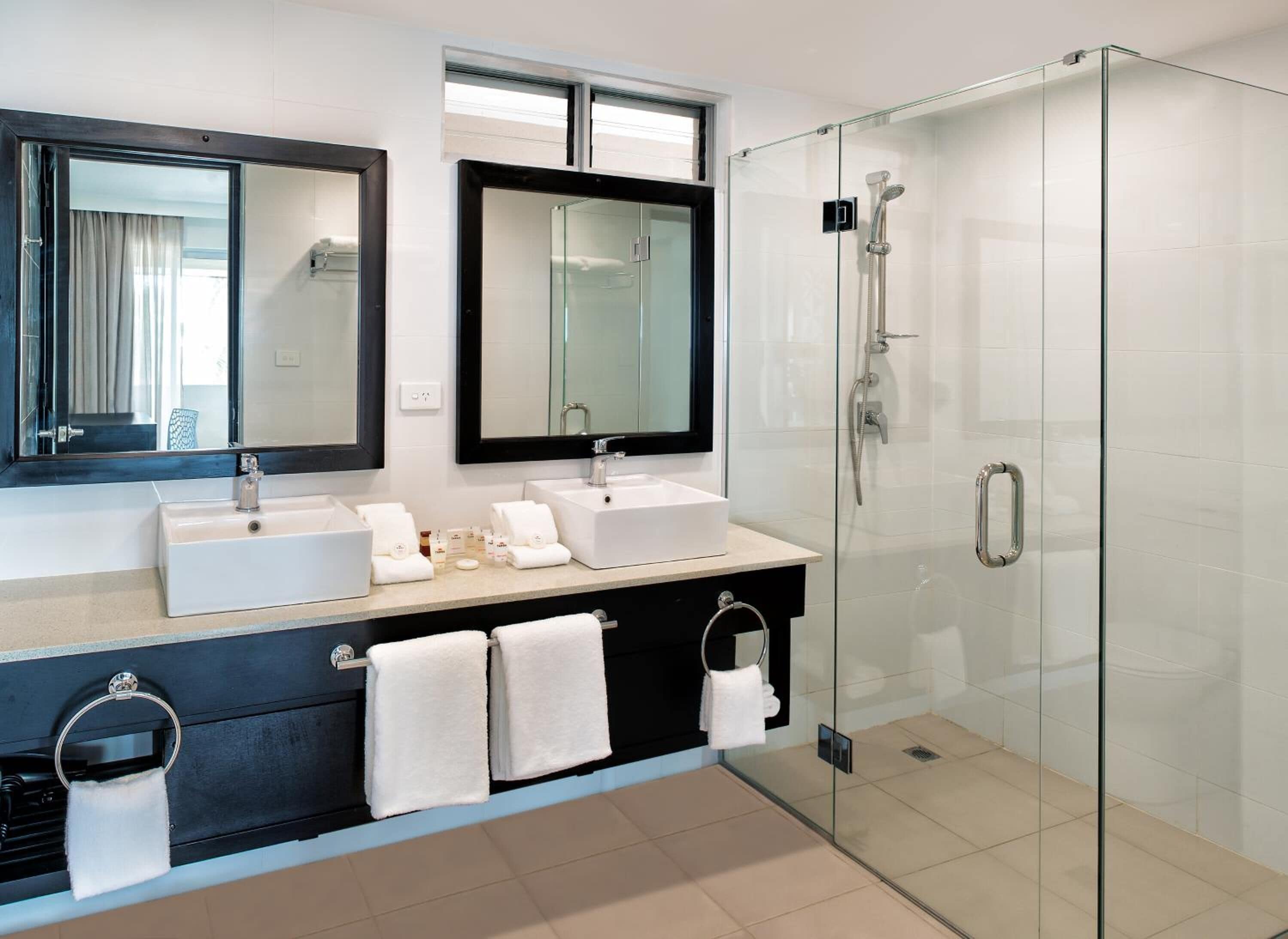 Un baño moderno con dos lavamanos, un espejo grande y una ducha con mampara de vidrio.