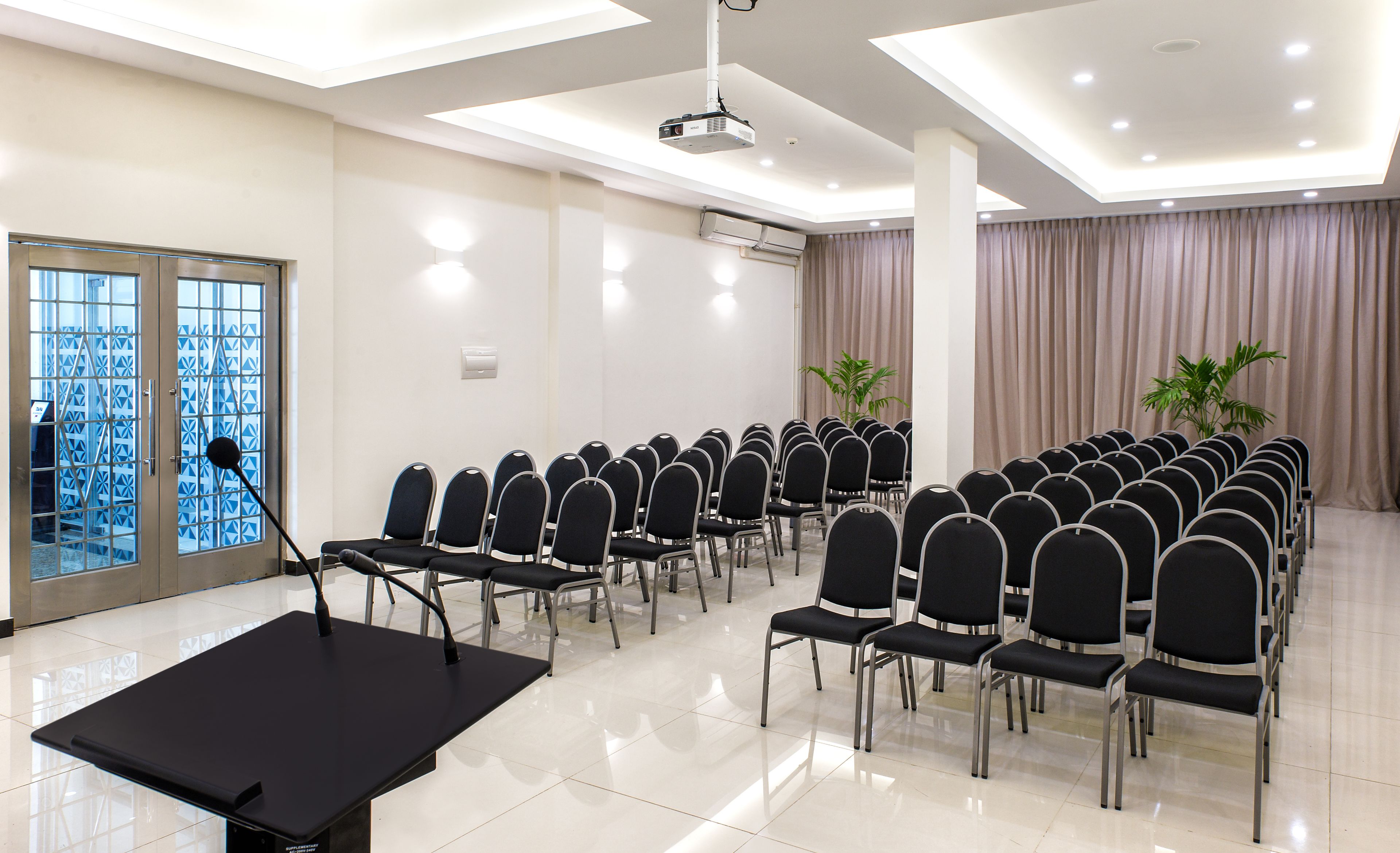 A conference room with rows of black chairs, a projector, and a large table.