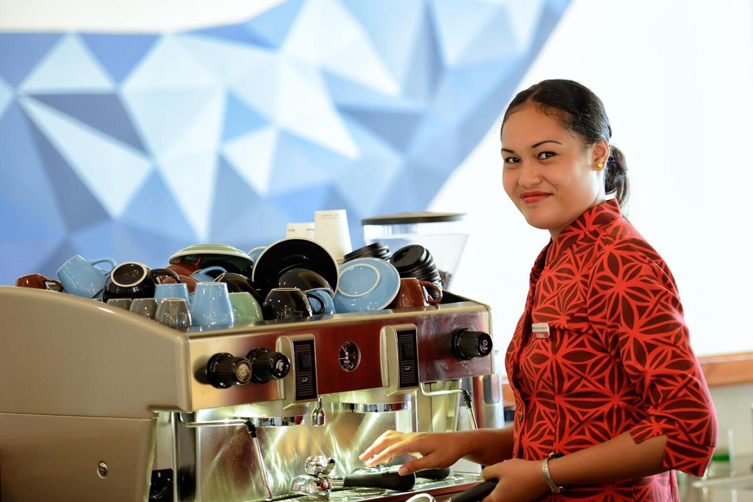 Una persona usando una máquina de café, con varias tazas y platillos apilados encima.