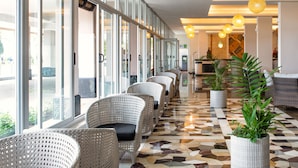 A hotel lobby with a row of wicker chairs, large windows, and potted plants.