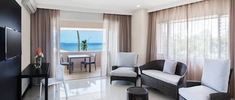 A modern living room with a balcony overlooking the sea, furnished with a sofa, chairs, and a small table.