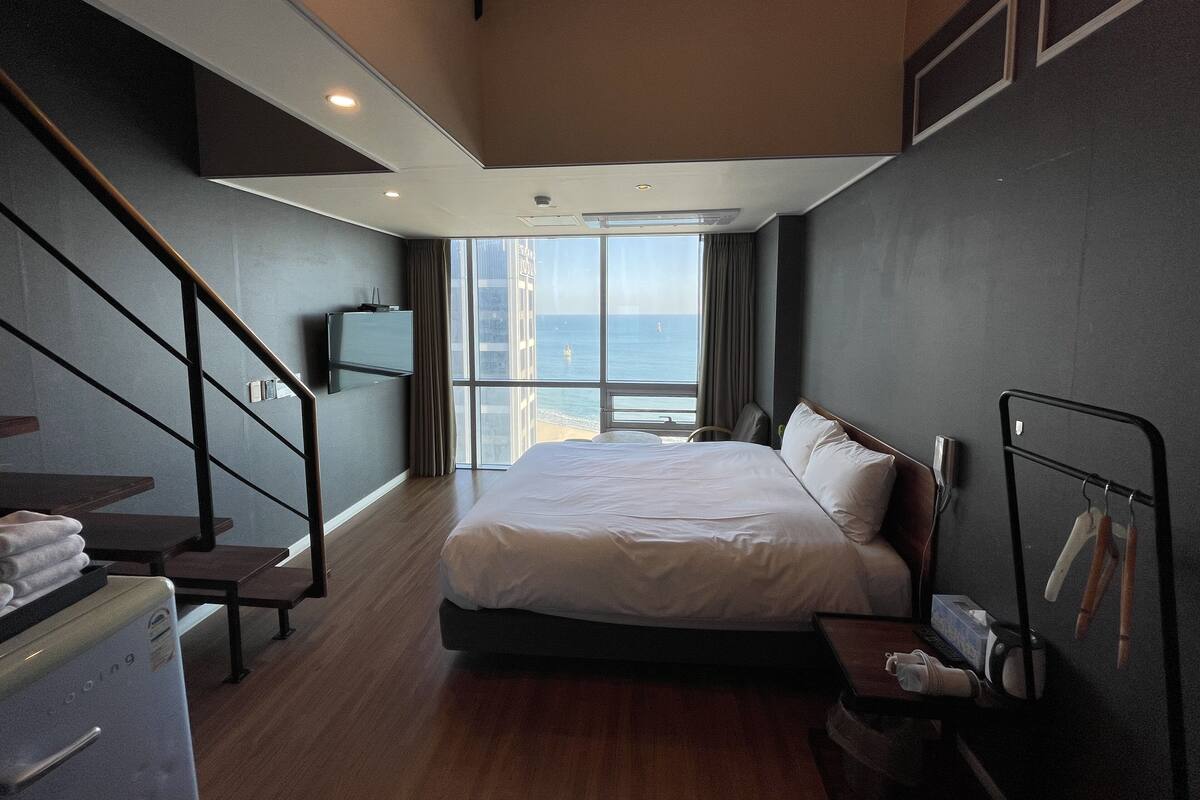 A hotel room with a bed, a desk, a chair, a TV, and a view of the ocean.