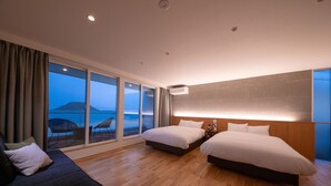 A hotel room with two beds, a sofa, a large window with a view of the sea, and a wooden floor. - Mizuno Ryokan (Karatsu)