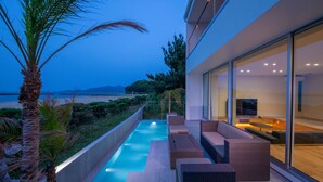 A modern outdoor pool area with seating, a view of the sea, and a large glass wall. - Mizuno Ryokan (Karatsu)