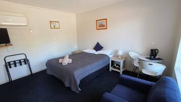 A hotel room with a bed, a desk, a chair, a TV, and a wall-mounted air conditioner.
