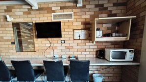 A small, modern kitchen with a brick wall, a flat-screen TV, a microwave, and a small shelf with kitchenware. - Red Chief Motel (Gunnedah)