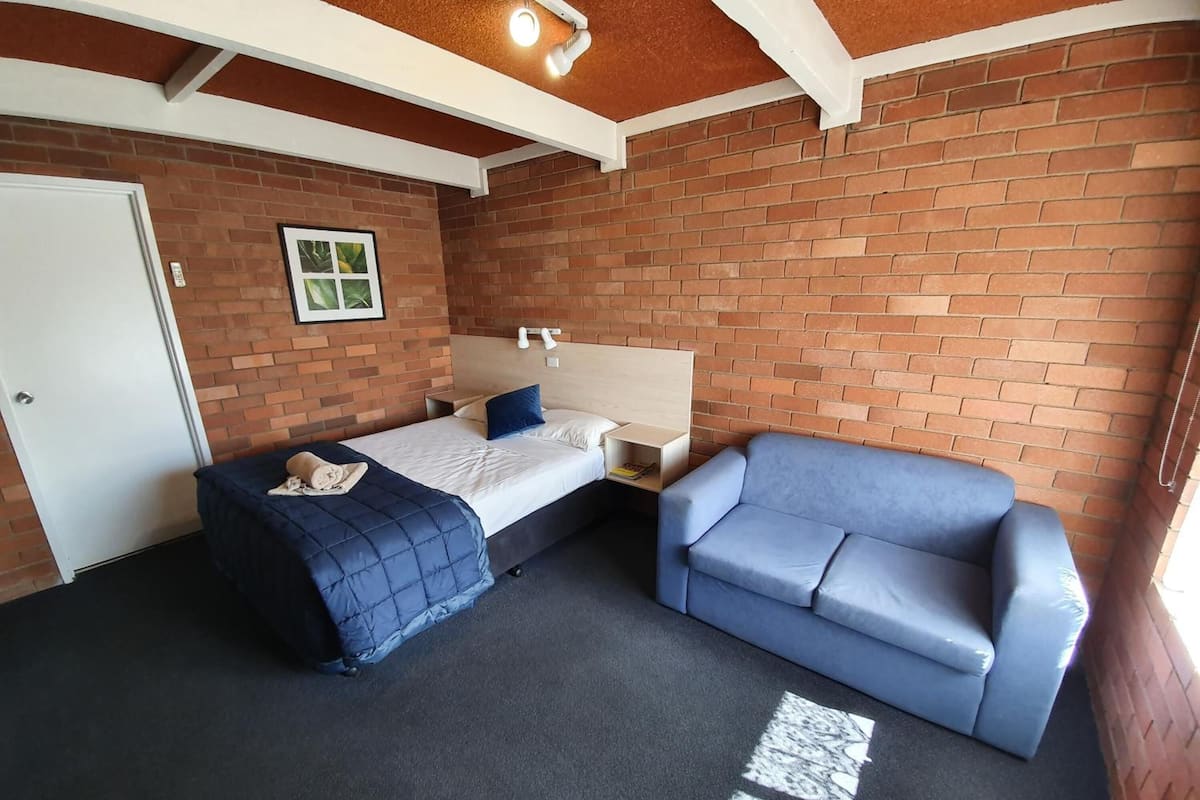 A room with a bed, a blue sofa, a white door, and a brick wall.