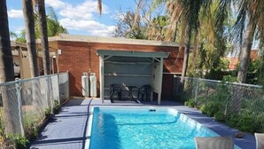 An outdoor swimming pool with a covered seating area and lounge chairs.