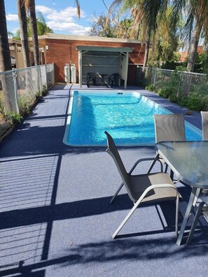Une piscine extérieure dotée d’un espace de repos couvert et de chaises longues.