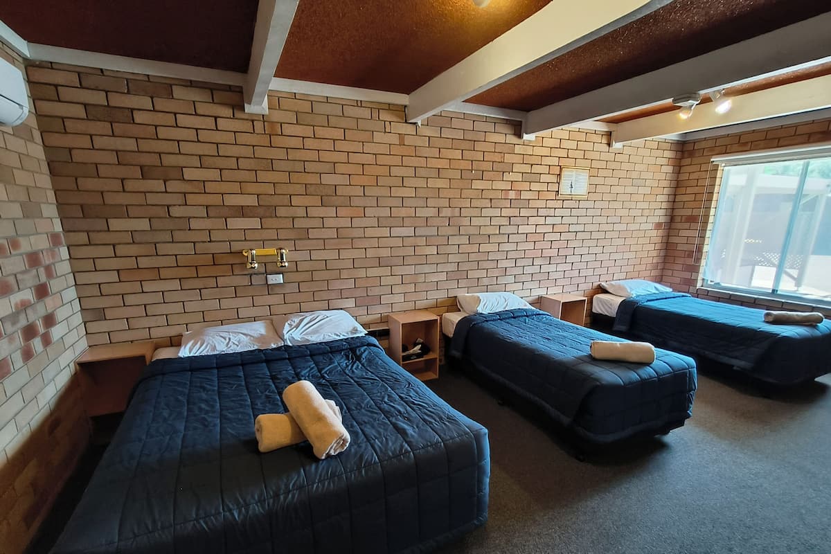 A hotel room with three beds, brick walls, and a window.