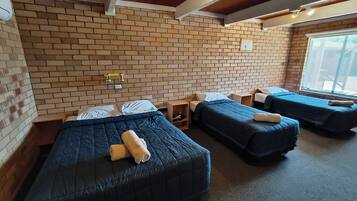A hotel room with three beds, brick walls, and a window.