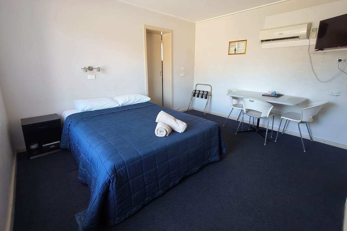 A hotel room with a bed, a desk, and a TV.