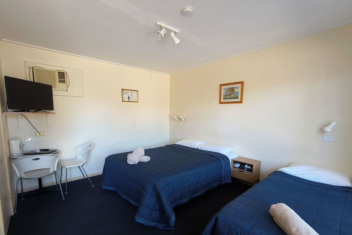 A hotel room with two beds, a desk, a chair, a television, and a wall-mounted air conditioner.