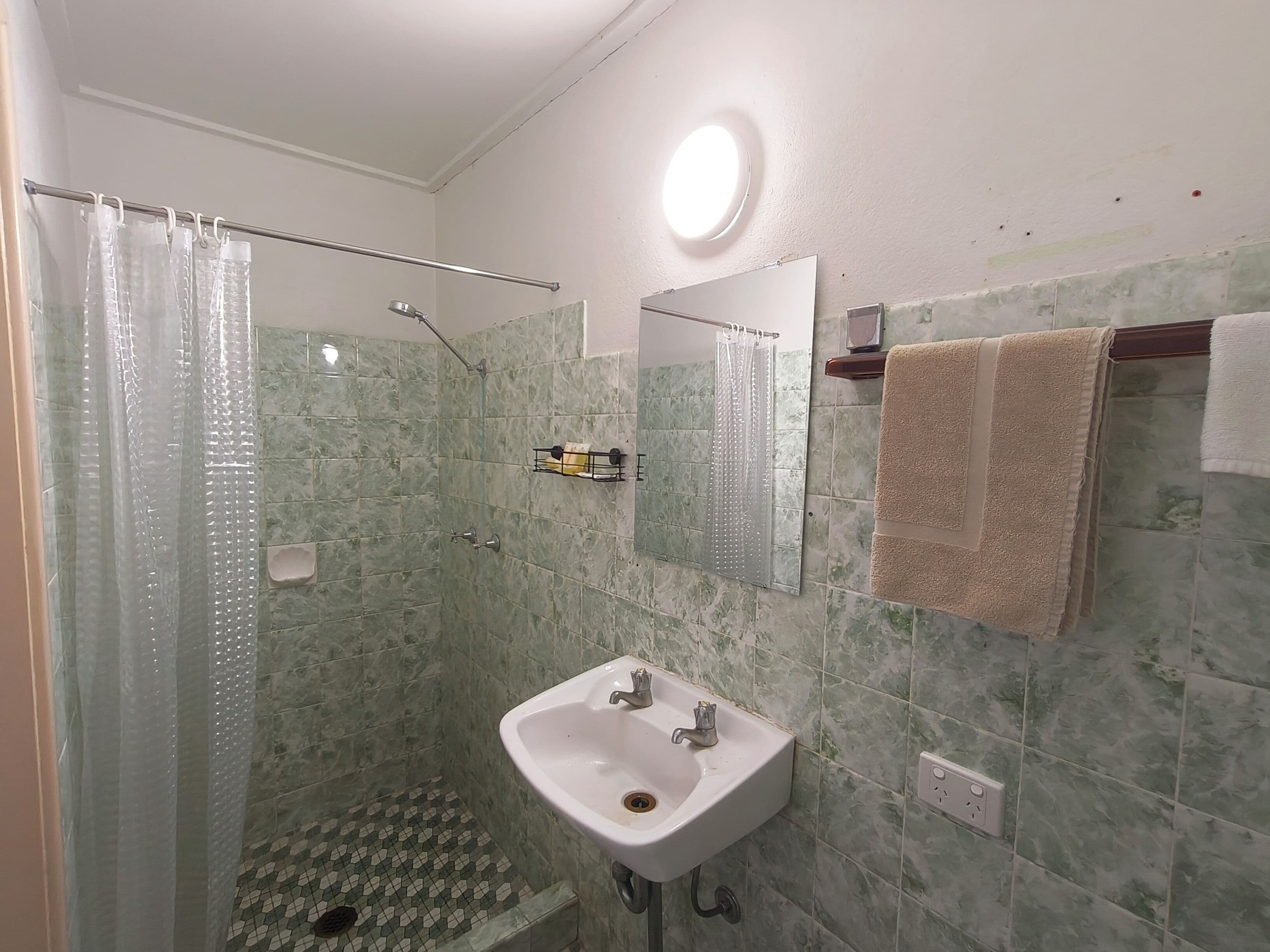 A bathroom with a shower, a sink, a mirror, and a towel rack.