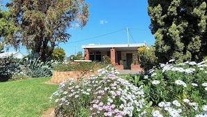 A house with a front yard, a large tree, and a garden with white and pink flowers. - Red Chief Motel (Gunnedah)