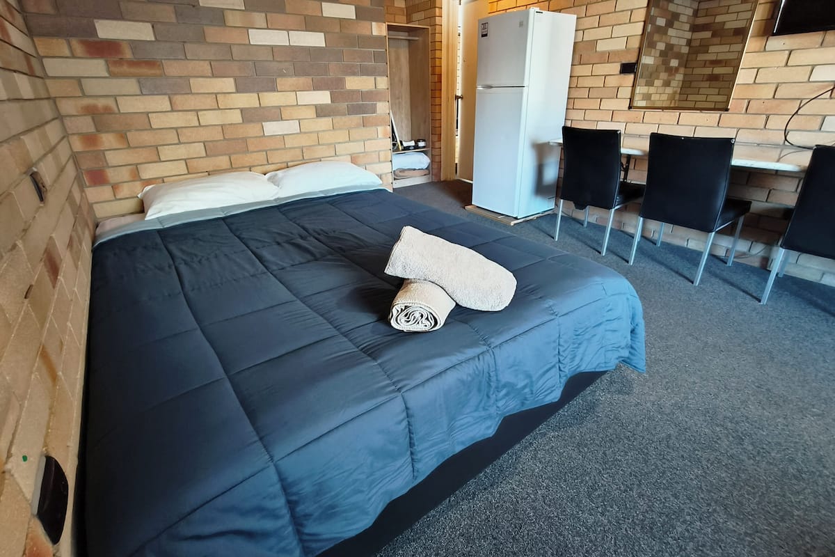 A hotel room with a bed, a desk, a chair, and a refrigerator.