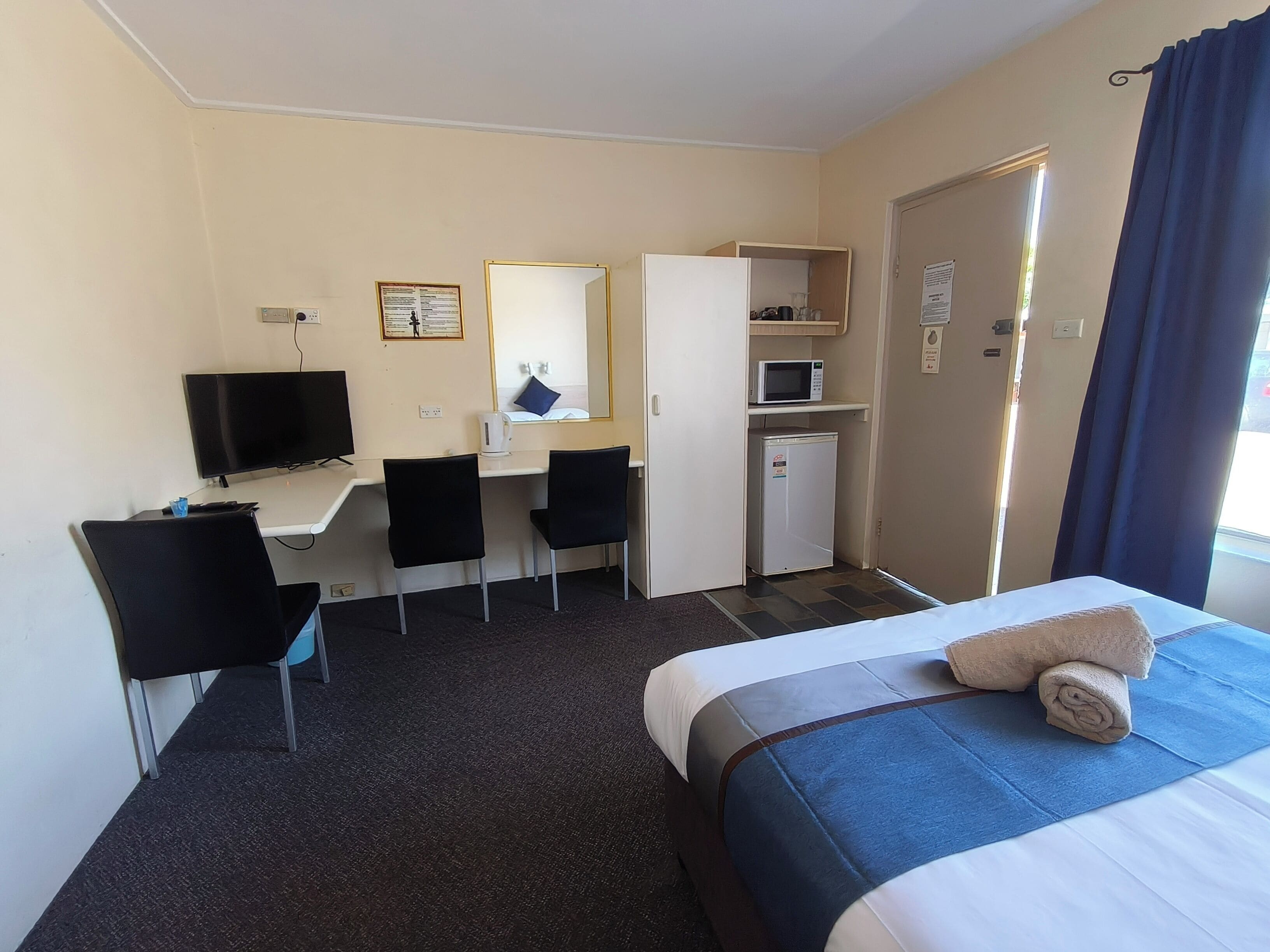 A hotel room with a bed, a desk with a computer, a microwave, and a small refrigerator.