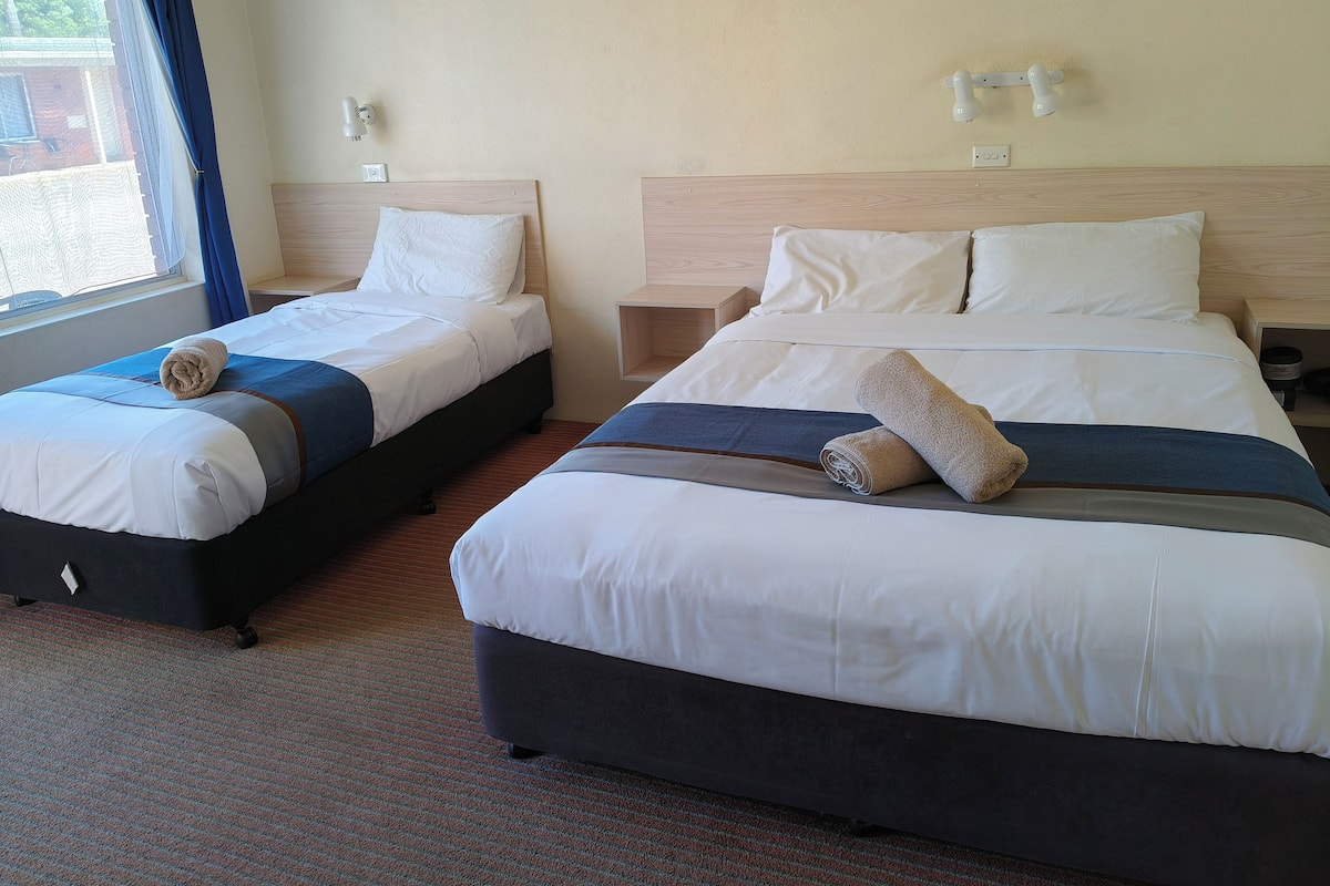 Two double beds with white linens, a wooden headboard, and a small bedside table with a lamp.